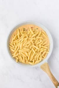 Adding cooked penne to a skillet of creamy sauce.