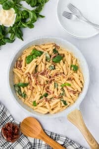 A skillet filled with sundried tomato penne, topped with parmesan and fresh basil.