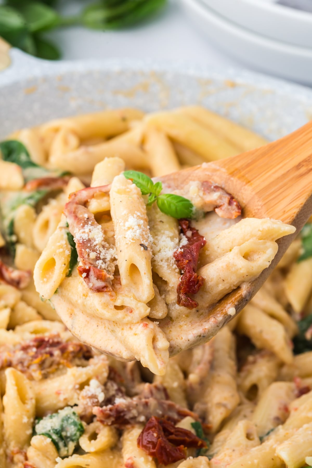 A wooden spoon taking a portion of pasta from a skillet.