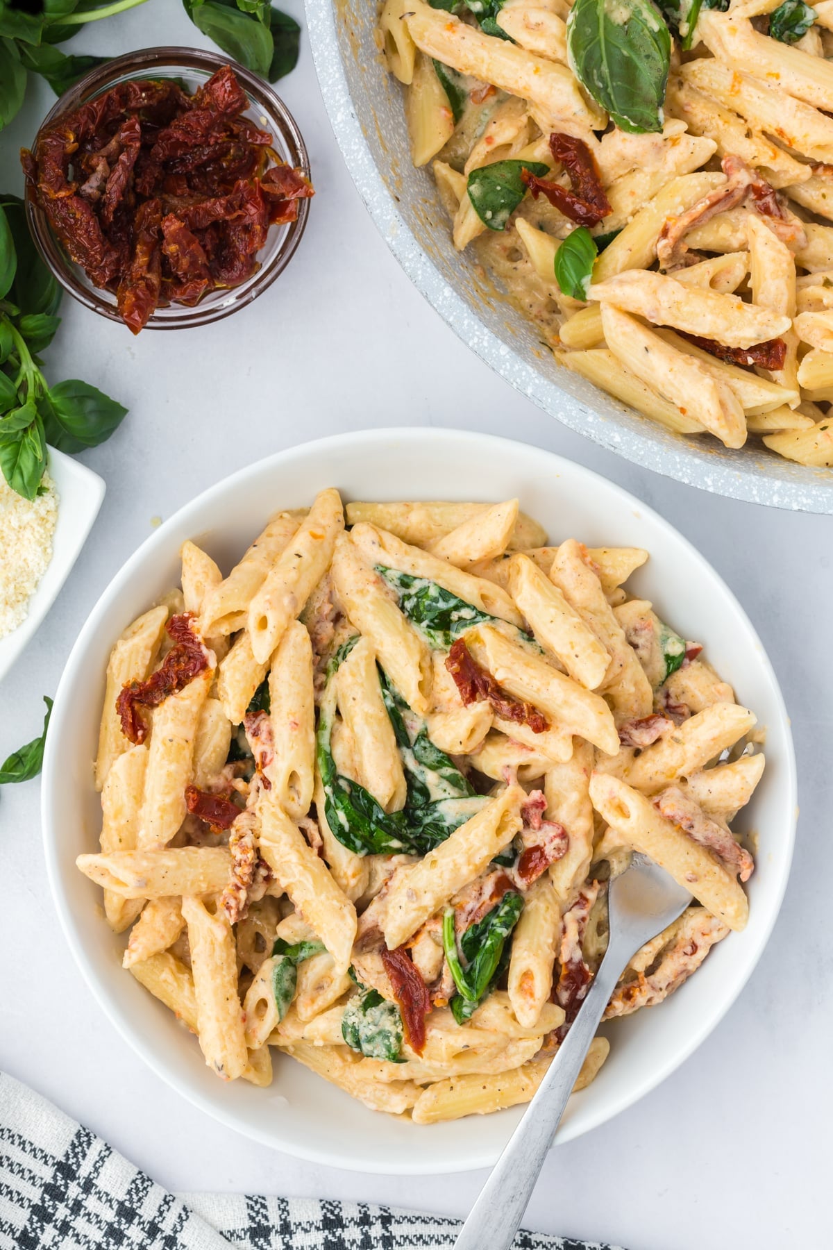 A bowl of creamy penne pasta featuring sundried tomatoes and spinach.