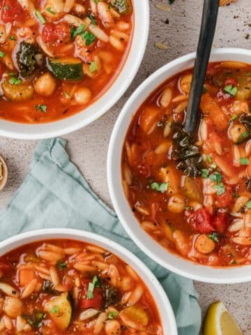 Bowls of soup with vegetables, orzo, and chickpeas.
