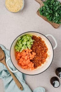 Adding celery and carrots to a Dutch oven.
