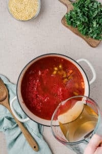 Pouring broth and tomatoes into a Dutch oven.