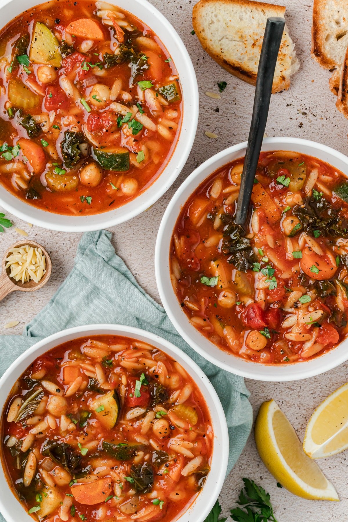 Three bowls of vegetable soup with orzo and kale.