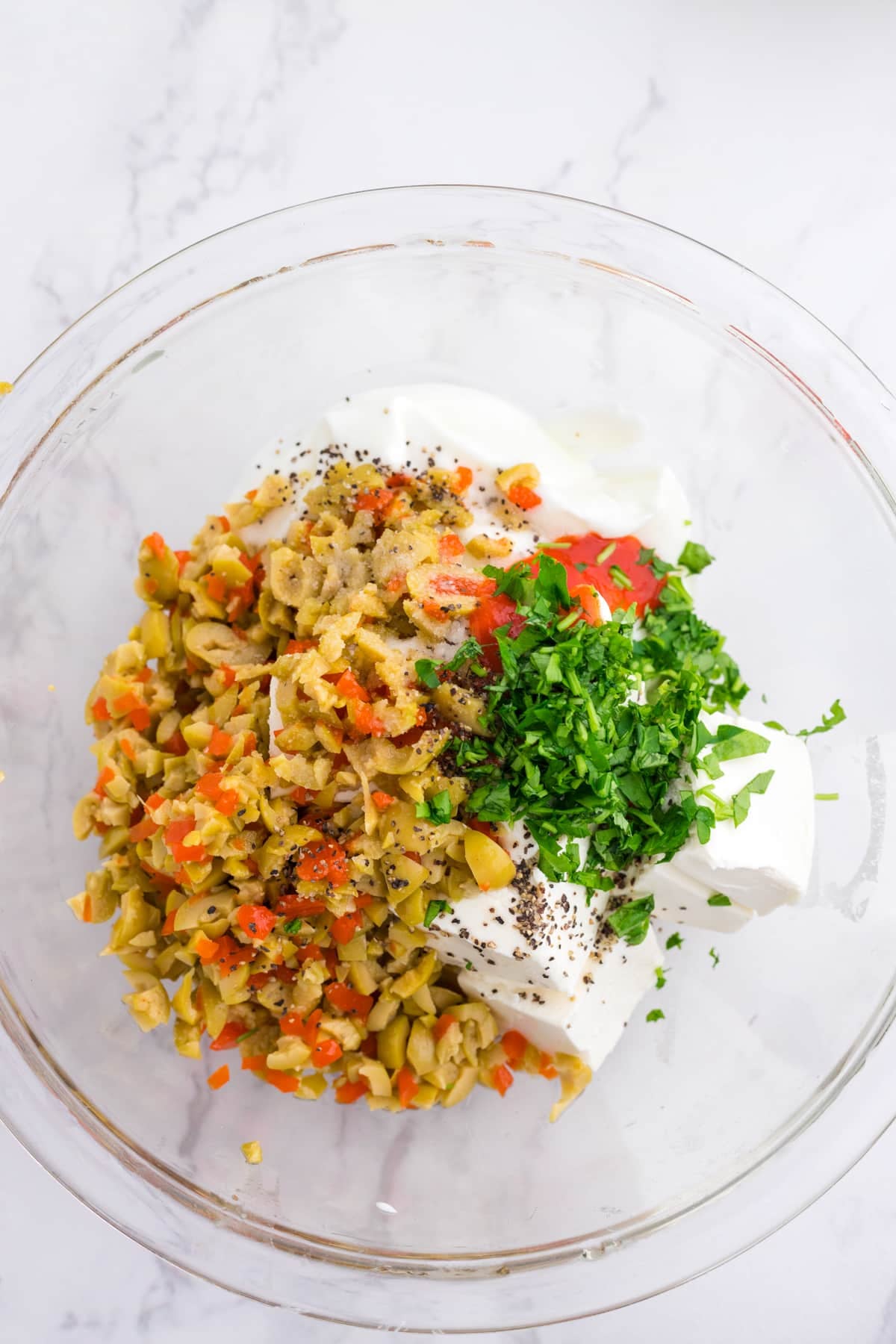 A mixing bowl with cream cheese, chopped olives, parsley, sour cream and seasonings.