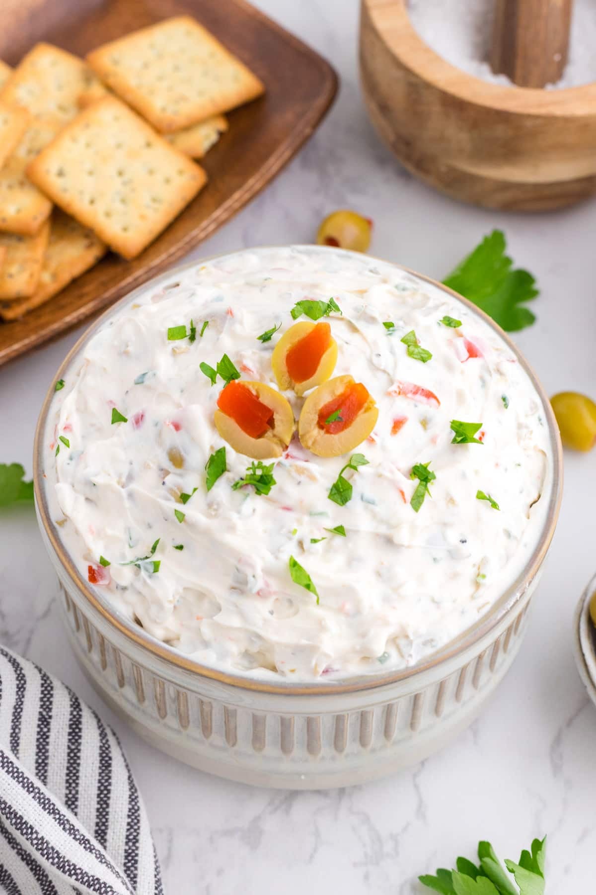 A bowl of dip topped with sliced olives and garnished with parsley.