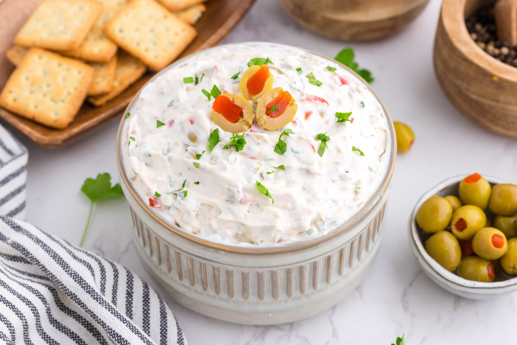 A small bowl of olive dip topped with sliced olives and garnished with parsley.
