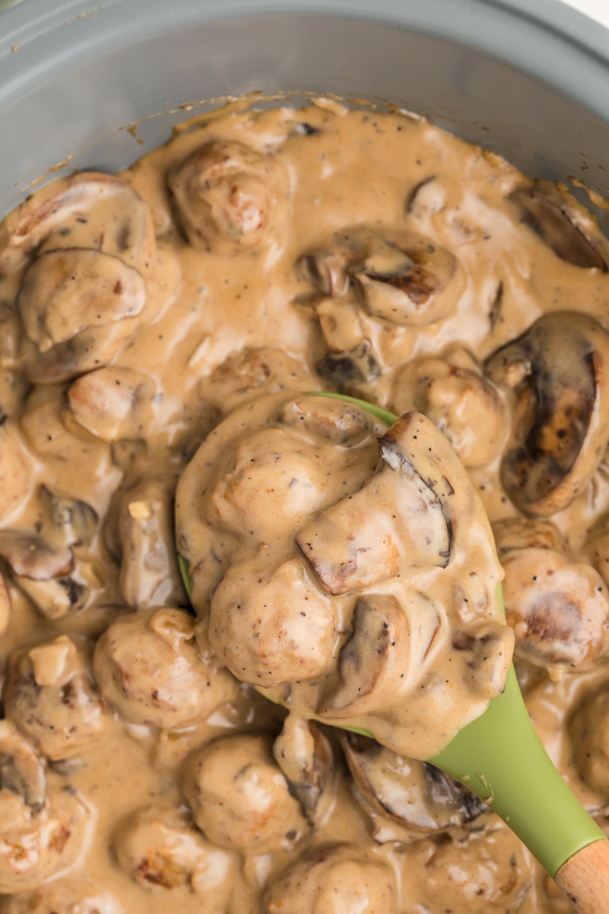 A spoon taking a portion of creamy mushroom meatballs from a skillet.