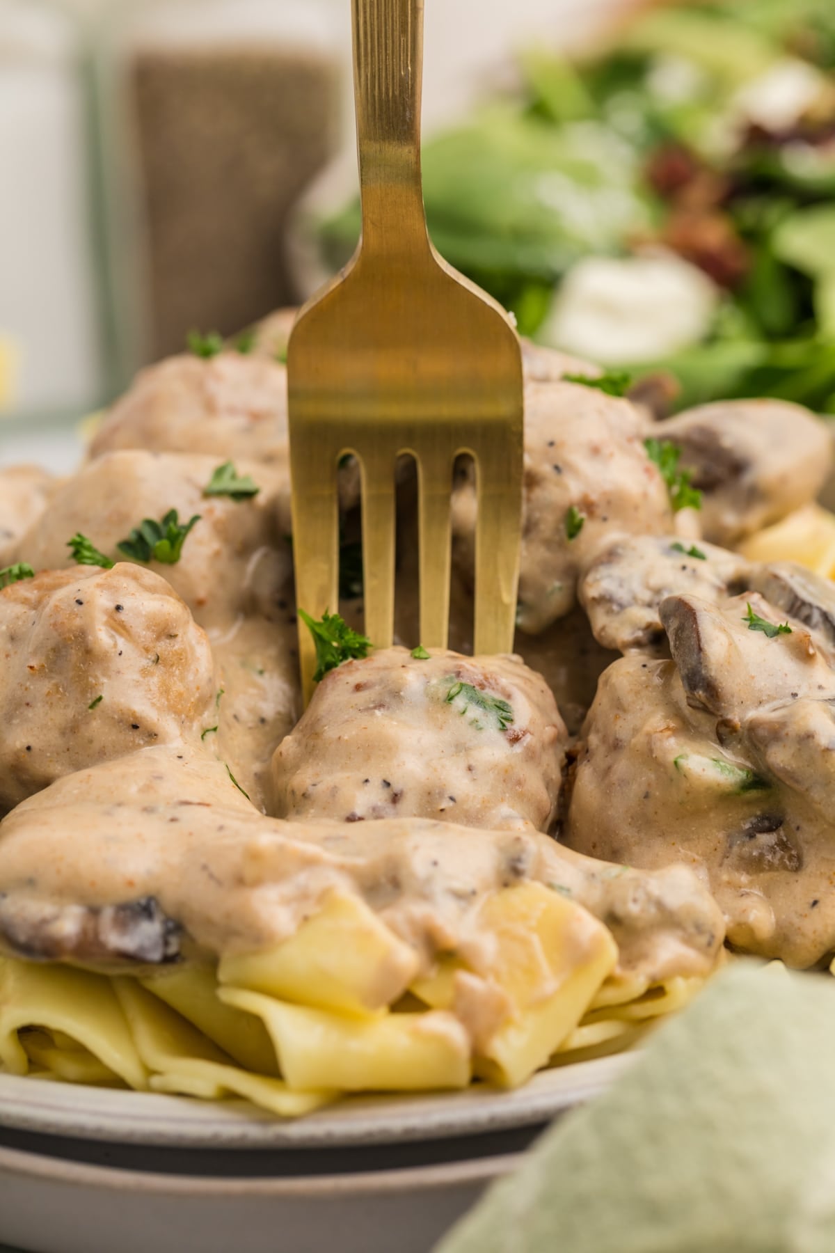 A fork piercing into a meatball on a plate of egg noodles and cream sauce.