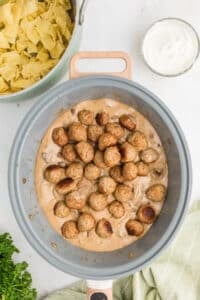 Adding meatballs to a creamy sauce in a large skillet.