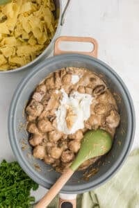 A skillet with meatballs in cream sauce, with sour cream being stirred in.