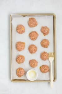 Brushing meatballs with olive oil on a baking sheet.