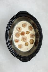 Adding meatballs to a cream sauce in a slow cooker.