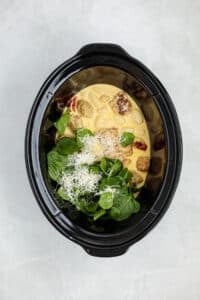 Adding spinach and parmesan cheese to a slow cooker cream sauce with chicken meatballs.