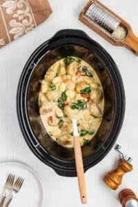 A slow cooker filled with gnocchi and chicken meatballs in a cream sauce with spinach and sundried tomatoes.