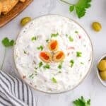 A small bowl of olive dip topped with sliced olives and garnished with parsley.