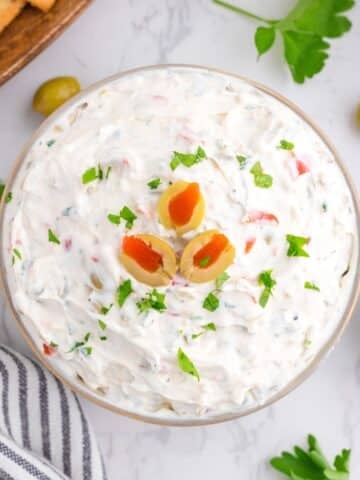 A small bowl of olive dip topped with sliced olives and garnished with parsley.