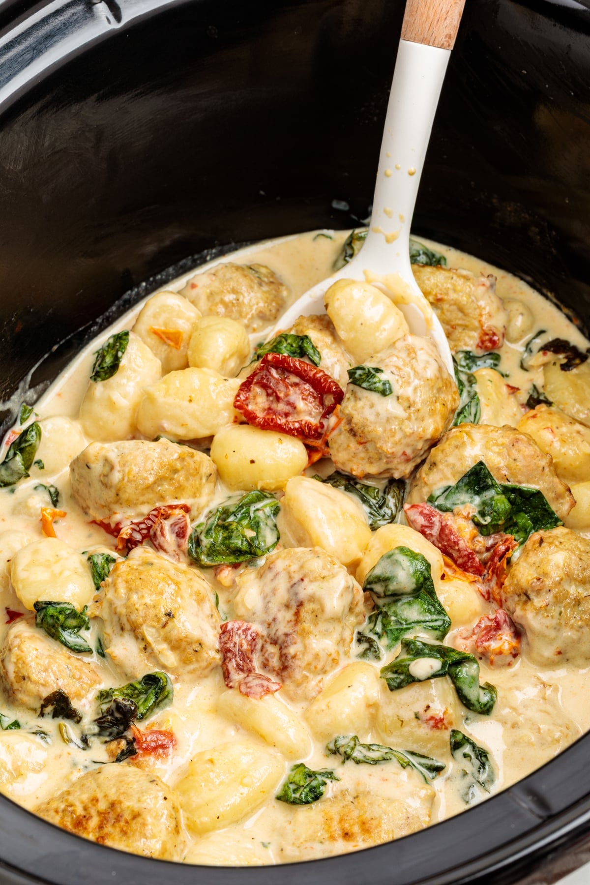 Scooping creamy chicken meatballs and gnocchi from a slow cooker.