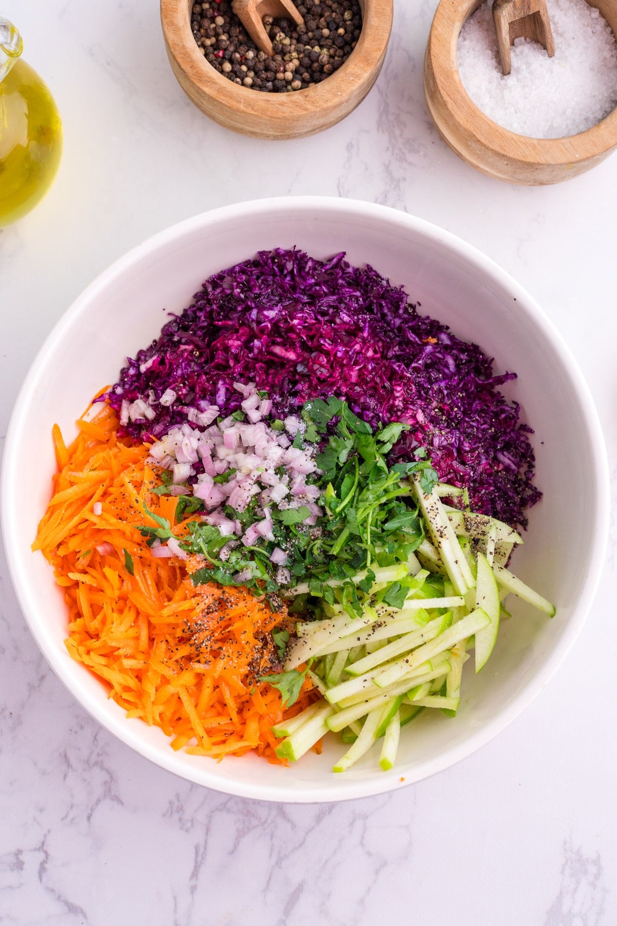 A white bowl with sections of red cabbage, shallot, carrots, apple, and parsley.