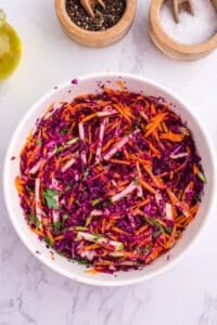 A white serving bowl with cabbage and carrot slaw, dressed with olive oil.