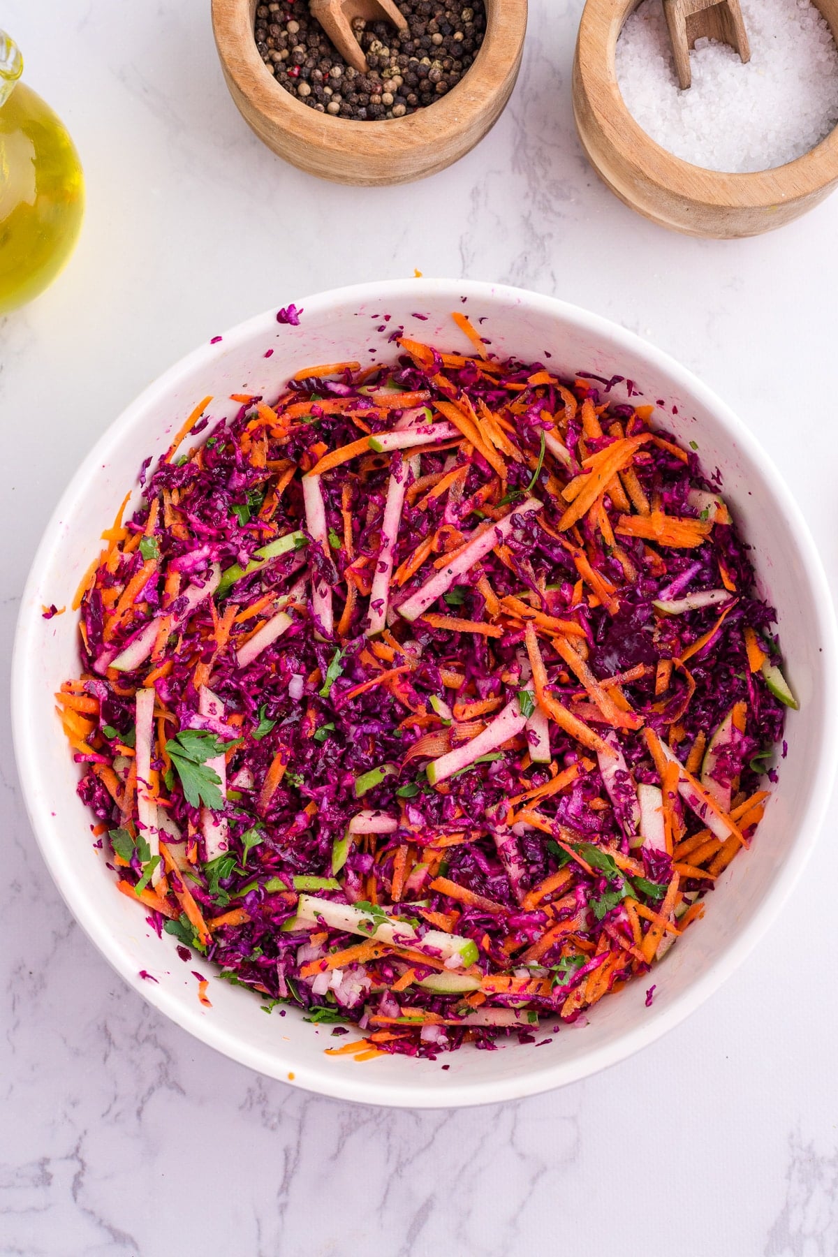 A white serving bowl with cabbage and carrot slaw, dressed with olive oil.