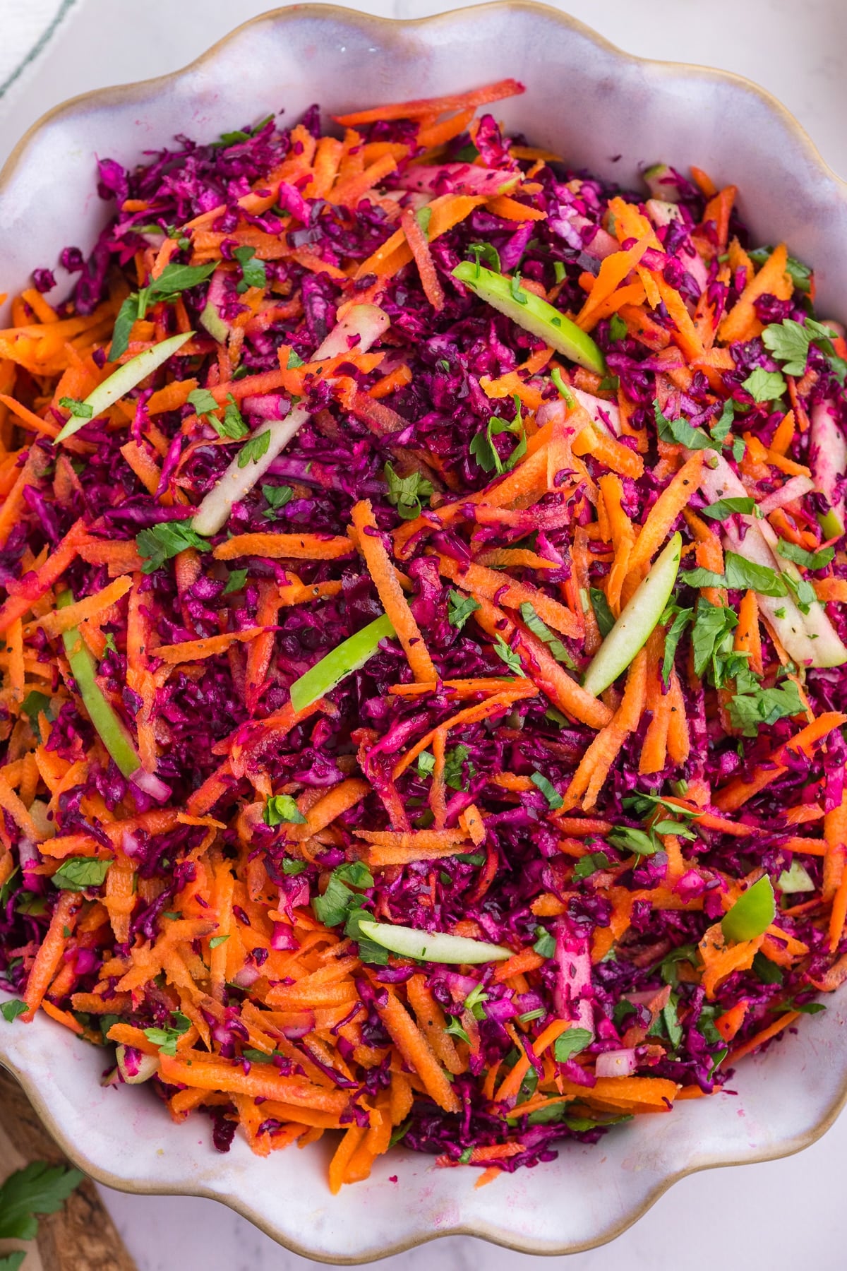 Cabbage and carrot slaw with green apple and parsley in a serving bowl.
