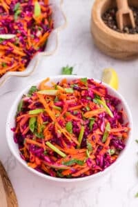 A bowl of cabbage and carrot slaw, garnished with fresh parsley.