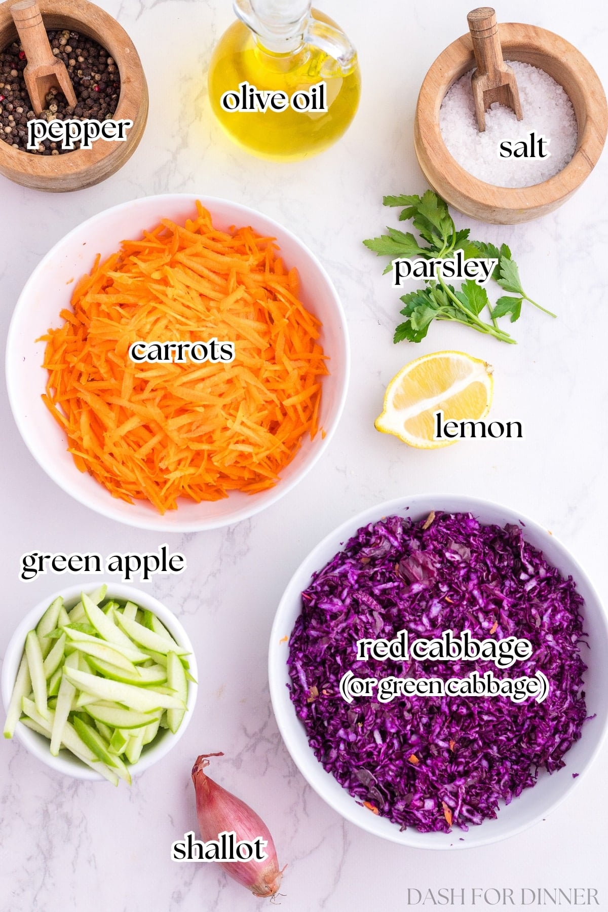 The ingredients needed to make cabbage and carrot salad, including shredded vegetables, apple, parsley, lemon, and olive oil.