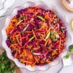 A bowl of cabbage and carrot salad garnished with parsley and green apple.