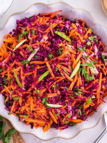 A bowl of cabbage and carrot salad garnished with parsley and green apple.