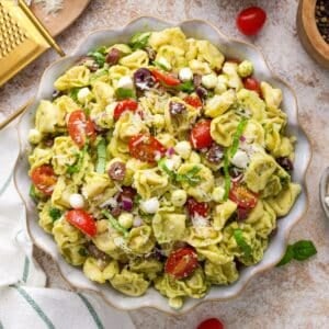 A bowl of pasta salad featuring tortellini, pesto, cherry tomatoes, and mozzarella.