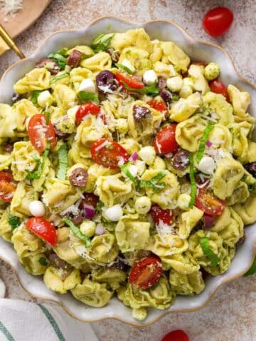 A bowl of pasta salad featuring tortellini, pesto, cherry tomatoes, and mozzarella.