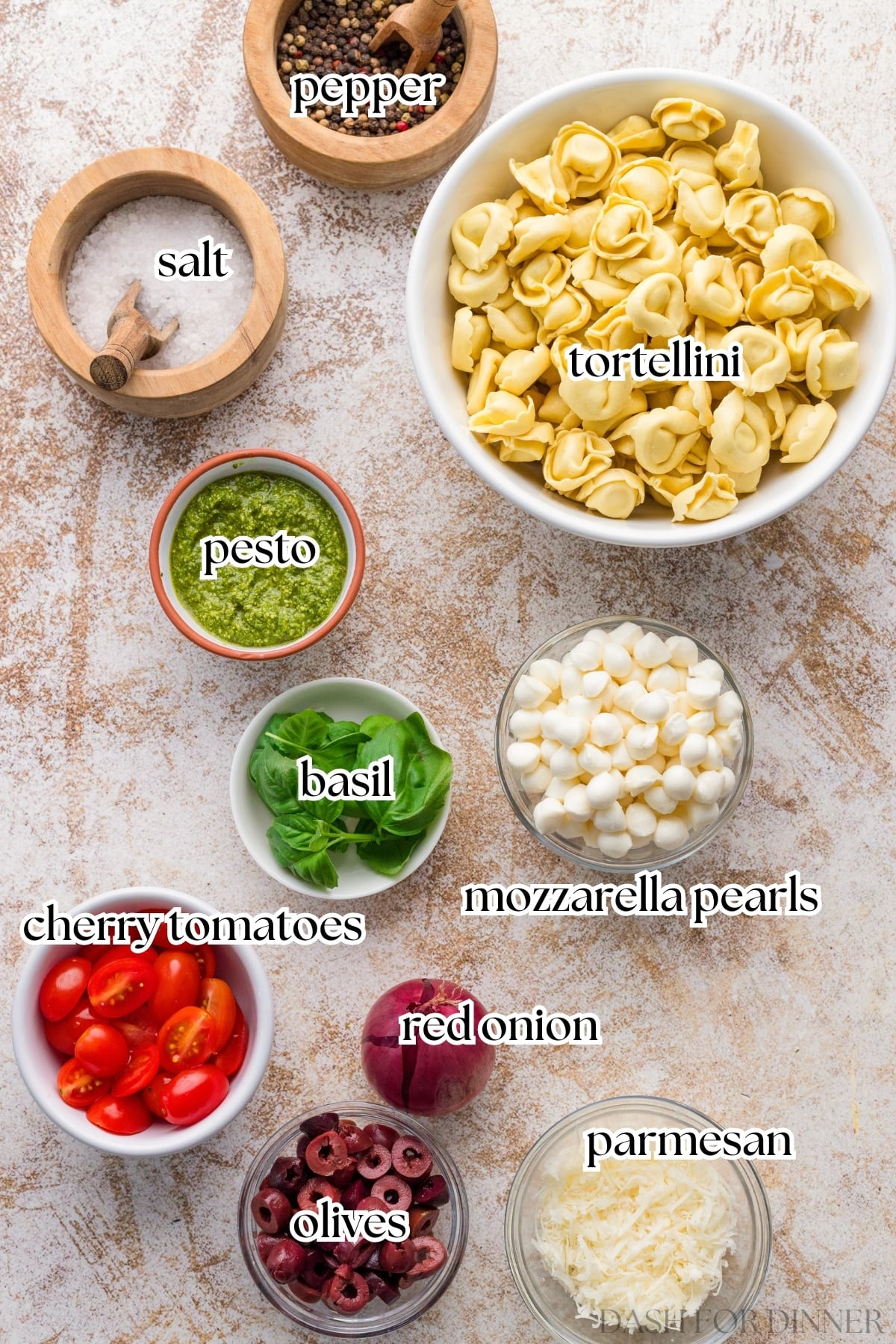 The ingredients needed to make tortellini pasta salad, including basil, red onion, and mini mozzarella pearls.