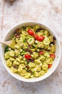 A bowl of cold tortellini salad tossed with basil pesto.