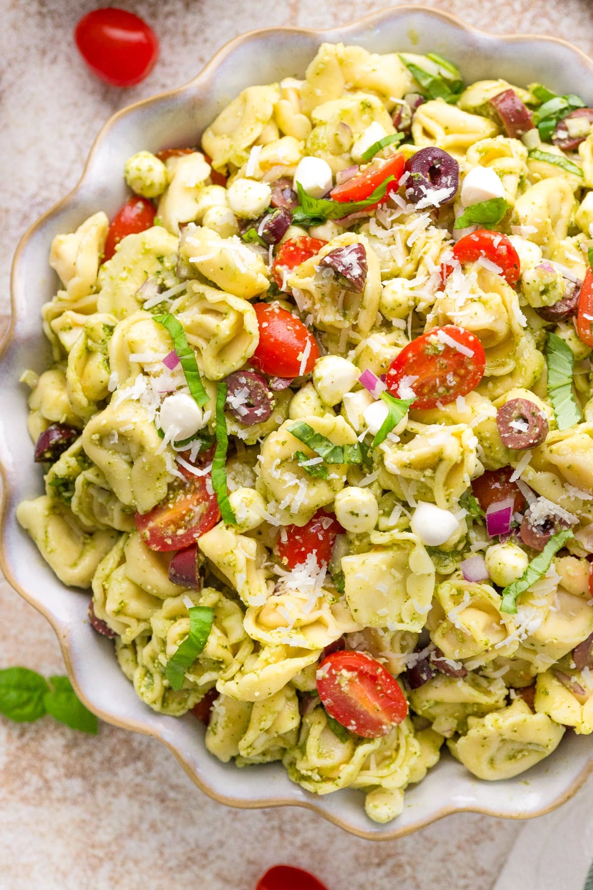 A salad bowl filled with cold tortellini salad, featuring cherry tomatoes, olives, and mozzarella.