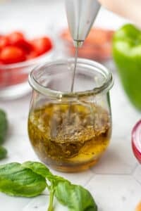 Using a mini frother to combine a homemade vinaigrette in a glass jar.