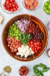 A salad bowl featuring multiple types of chopped veggies and pizza toppings arranged like a wheel in a salad bowl.