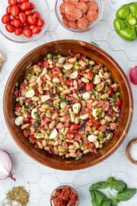 A bean salad with mozzarella balls, pepperoni, and veggies i a wooden salad bowl.