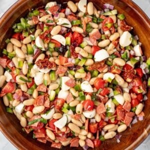 A bowl of bean salad with veggies, pepperoni, and mini mozzarella balls.