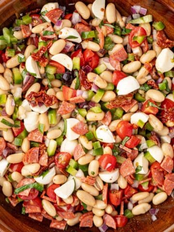 A bowl of bean salad with veggies, pepperoni, and mini mozzarella balls.