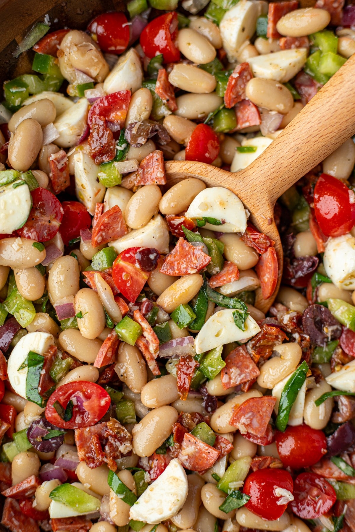 A wooden spoon taking a portion of pizza bean salad from a bowl.