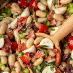 A wooden spoon taking a portion of veggie packed bean salad with pepperoni and mozzarella.