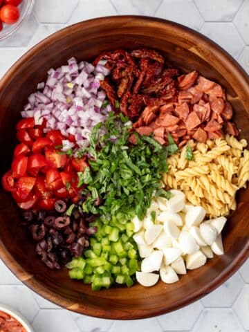 A salad bowl filled with compartments of pasta, mozzarella, green pepper, red onion, pepperoni, etc.