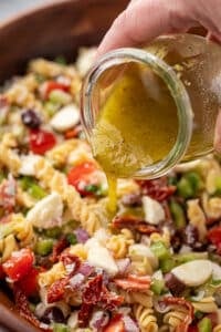 Pouring salad dressing over a pasta salad in a bowl.