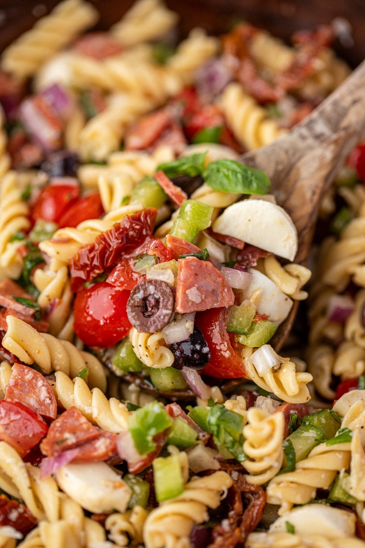 A wooden spoon taking a portion of pasta salad from a family size amount.