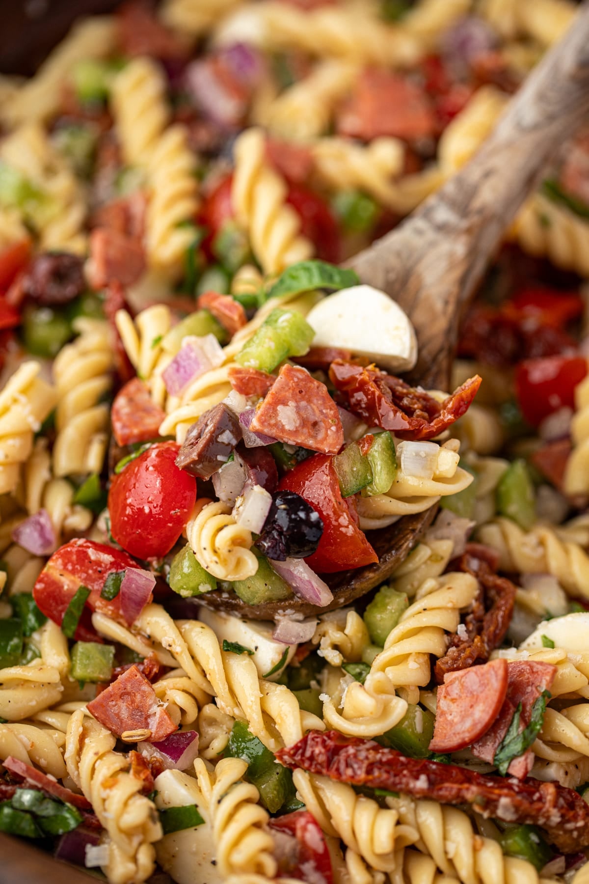 A wooden spoon taking a portion of pasta salad from a bowl.
