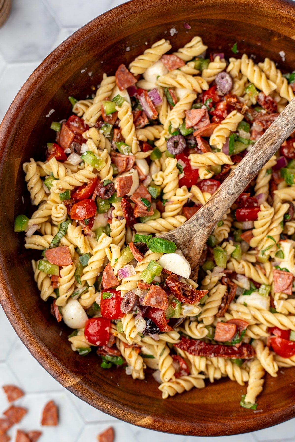 A wooden salad bowl filled with pasta salad featuring sundried tomatoes, mozzarella, and pepperoni.