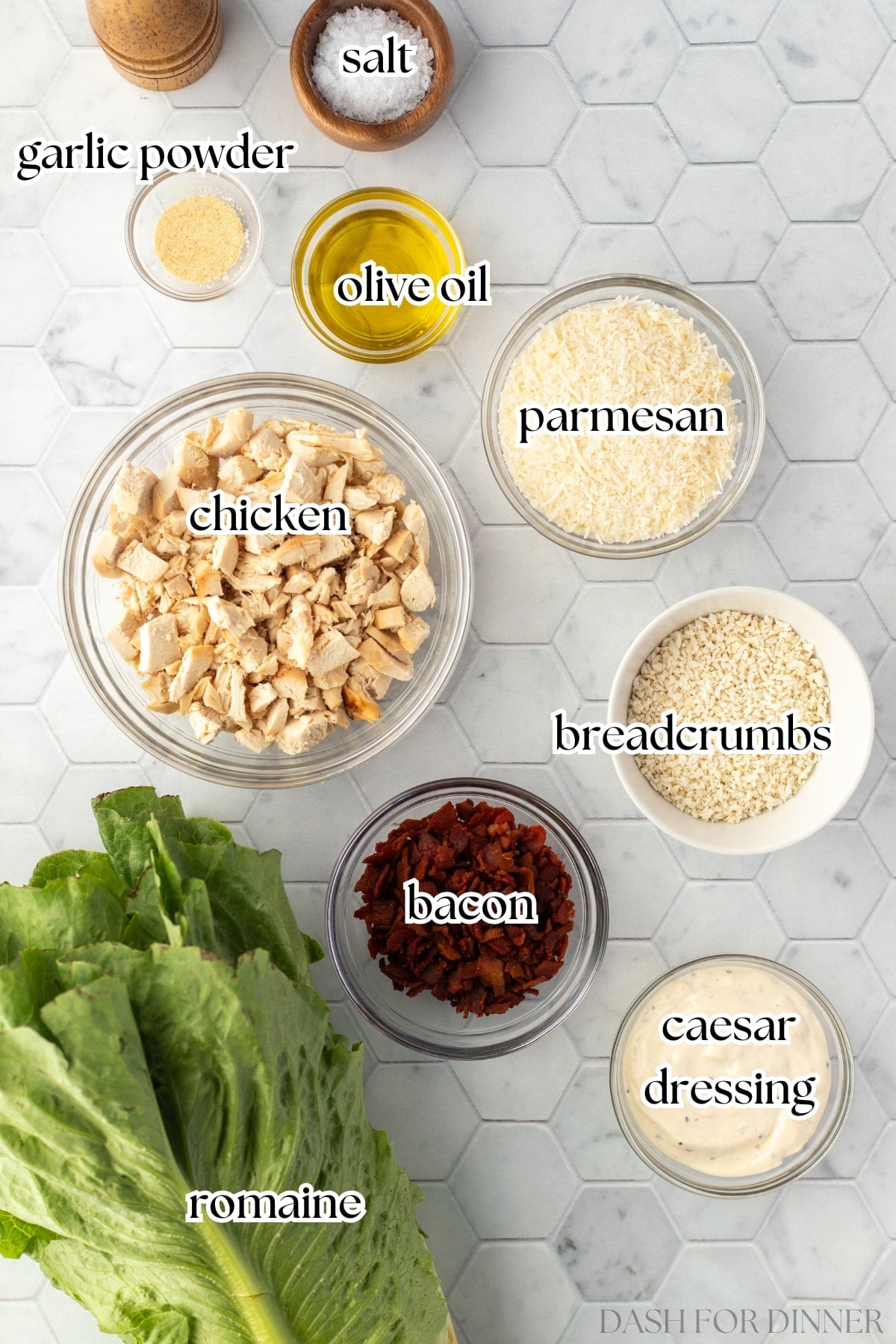 The ingredients needed to make chicken caesar salad, including romaine, breadcrumbs, parmesan, bacon, and caesar dressing.