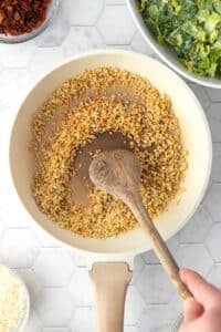 A skillet with breadcrumbs being toasted and stirred.