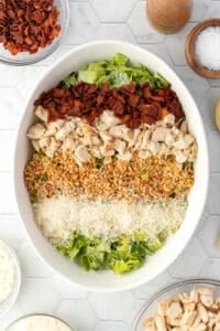 Adding bacon, chicken, breadcrumbs, and parmesan cheese to a large bowl of dressed romaine lettuce.